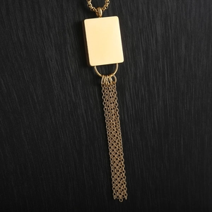 Macro shot of 18K gold plated long tassel pendant with square link chain over dark background