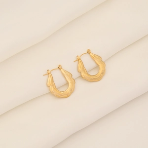 Minimalist golden U-shaped earrings with wave texture on a soft beige background