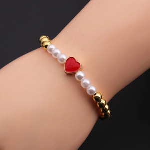 Detailed shot of golden beads and white pearl bracelet featuring a red heart pendant