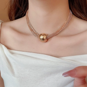 Detail of layered gold chain necklace featuring a polished metal ball pendant on a model
