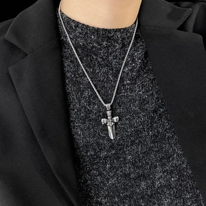 Close-up of a silver cross and dagger pendant necklace worn over a black jacket
