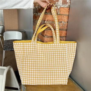 Macro shot of yellow plaid canvas tote bag being held against a minimalist background