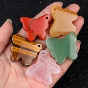 Set of five carved natural stone butterfly pendants held in hand with shiny black background