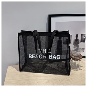 Close-up of black mesh tote bag featuring THE BEACH BAG text in a modern lifestyle setting