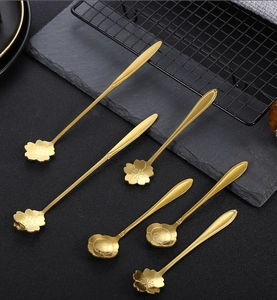 Detailed close-up of six gold stainless steel flower-shaped dessert spoons on slate