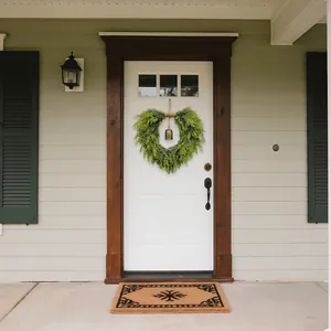 Christmas heart-shaped evergreen wreath with golden bell on a white front door