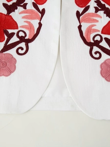 Detailed close-up of vibrant floral embroidery on a white blazer fabric with clear stitching