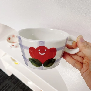 Detail showing the blue checkered pattern and red smiley flower on a white ceramic mug