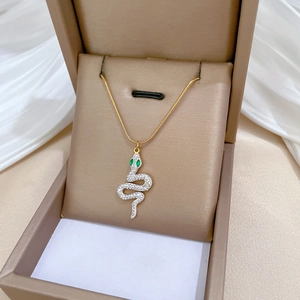 Detail of a gold snake necklace with green eye stones in a beige jewelry box