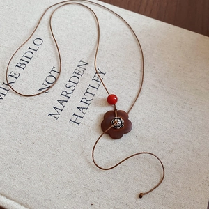 Détail d'un pendentif en bois fleuri avec perle rouge sur une cordelette tressée