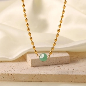 Macro shot of gold beaded necklace with a round green gemstone on silk backdrop