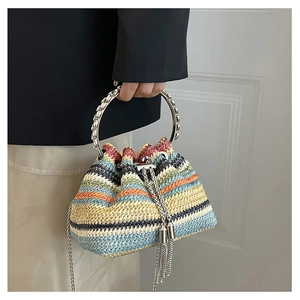 Dettaglio di una borsa a secchiello tessuta colorata con manici in metallo e nappe lunghe