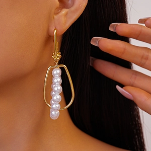 Detail of gold geometric hoop earrings with vertical faux pearls on a female model
