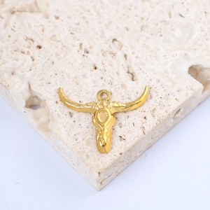 Macro shot of a golden bull skull pendant with ring on a textured beige stone surface