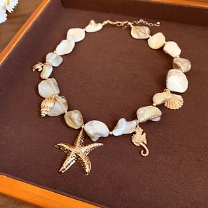 Collana con stelle marine e conchiglie e ciondoli dorati su vassoio di legno