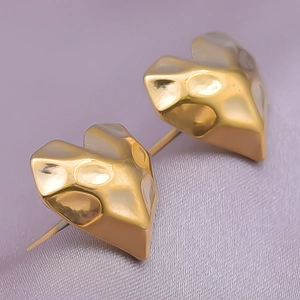Close-up of golden 304 stainless steel heart-shaped studs with textured finish on purple silk