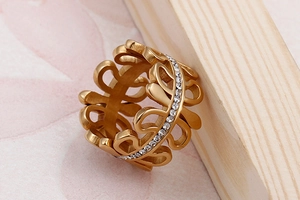Macro shot of gold leaf pattern ring with pavé crystals on textured wood background