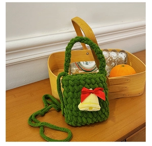 Detail of green knit reindeer bag with festive bell and red ribbon on wood surface