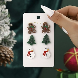 Close-up of Christmas stud earrings featuring gingerbread man, tree, and snowman designs