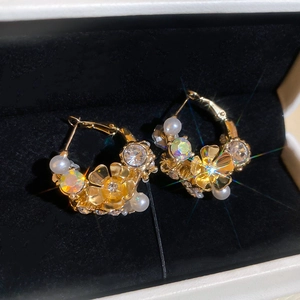 Close-up of golden floral hoop earrings with sparkling crystals and elegant pearls