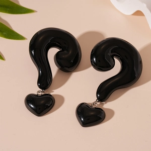 Detailed view of black resin heart and question mark earrings on beige backdrop
