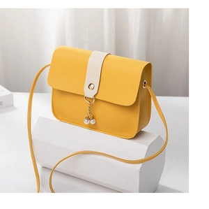 Detail of yellow crossbody bag with pearl charms on elegant white geometric stand