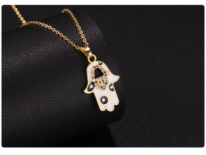 Macro shot of gold Hamsa pendant with white enamel and colorful inlaid gemstones