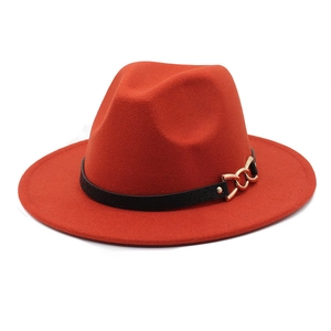 Detail view of brick red fedora hat featuring a black leather belt and gold chain buckle