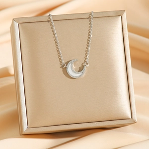 Silver crescent moon necklace with white shell inlay and diamonds on a gold box