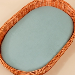 Detail of hand-woven wicker baby bassinet with soft morandi blue quilted cotton mattress
