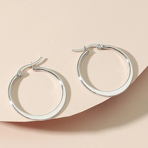 Polished silver stainless steel large hoop earrings displayed on a soft pink surface