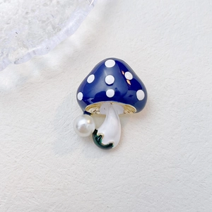 Détail d'une broche champignon en émail bleu à pois blancs et perle blanche élégante