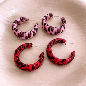 Close-up of retro C-shaped earrings with leopard print fabric wrap on ceramic plate