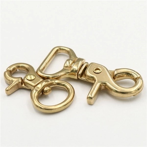 Macro detail of two polished brass lobster clasps with swivel D-rings on white background