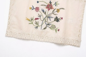 Detailed embroidery of colorful daisies and white lace trim on cream knit fabric