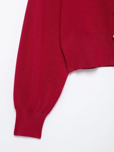 Detailed macro view of the red knit cardigan featuring ribbed cuffs and fine fabric texture