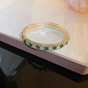 Macro detail of gold-plated bracelet with pavé-set white diamonds and green crystal emeralds