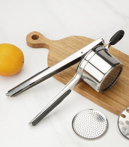 Close-up of stainless steel potato ricer with interchangeable discs on wooden board