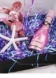 Iridescent purple shredded paper filler inside a black gift box with a plush bunny