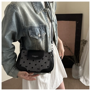 Détail d'un sac à bandoulière noir à pois avec nœud, porté par un mannequin en style chic