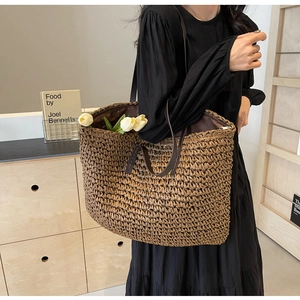 Detail of hand-woven straw tote bag with brown leather strap and secure zipper closure