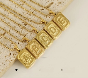 Détail de pendentifs lettres en acier doré 18K avec chaîne torsadée et finition polie