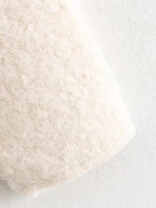 Close-up of thick cream curly faux fur texture on a warm winter cardigan sweater