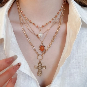 Detail of layered gold necklace with acrylic pearls, orange gems, and a textured cross