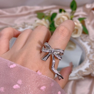 Close-up of sparkling zircon bow ring on hand with pink silk and vintage mirror background