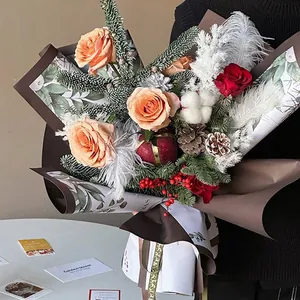 Christmas bouquet with roses and pine cones wrapped in Santa themed paper held by hand