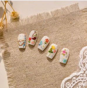 Dettaglio macro di adesivi per unghie con fiori 3D e cuori effetto ricamo su lino grezzo
