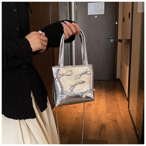 Detail view of silver handbag featuring metallic finish and 3D bowknot decorations