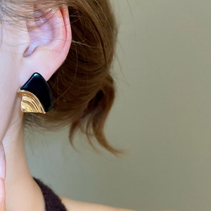 Close-up of geometric black and gold textured earrings worn by a model in profile view