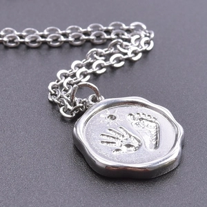 Detailed close-up of a silver stainless steel pendant with handprint and sun engraving